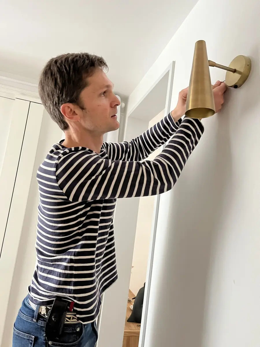 Quentin fixe une applique murale en laiton dans un couloir d’appartement à Paris